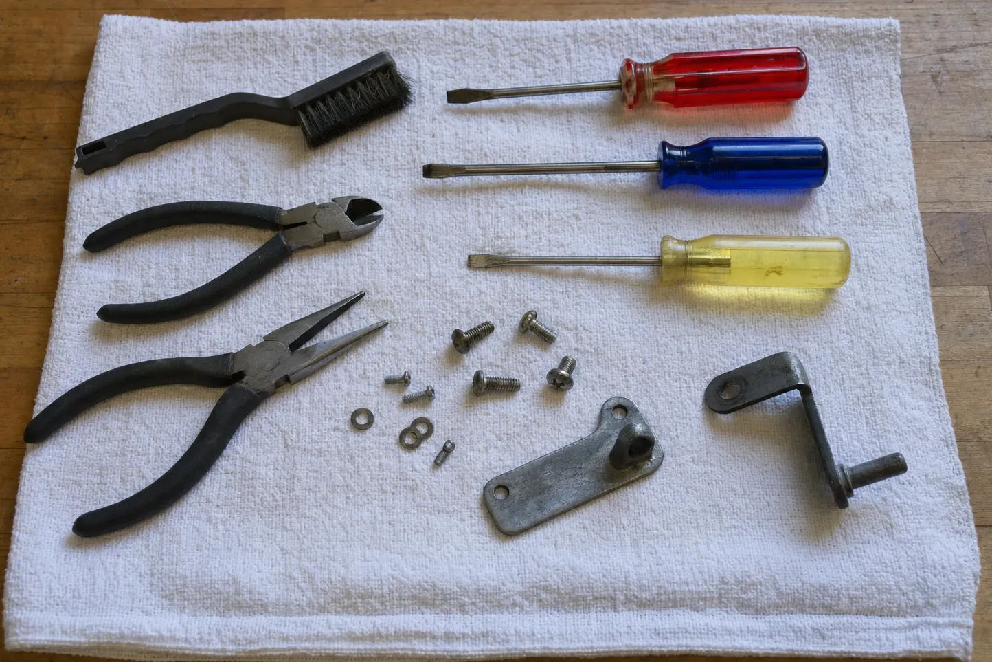 Screwdrivers, pliers, a wire brush, loose screws and two steel brackets laid out on a folded white towel